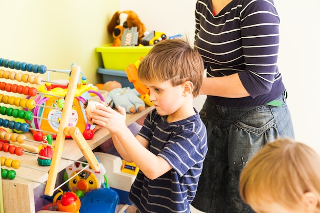 Photo la maman range les jouets et apprend au petit enfant à nettoyer dans la salle de jeux