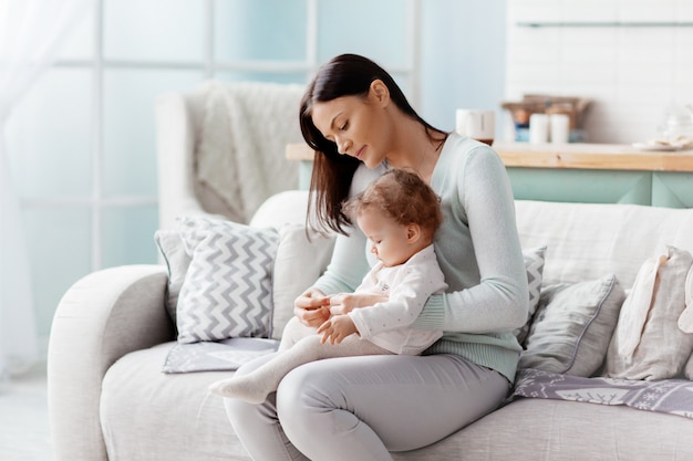 Maman s'assoit sur le canapé, tient son bébé sur ses genoux, met des vêtements