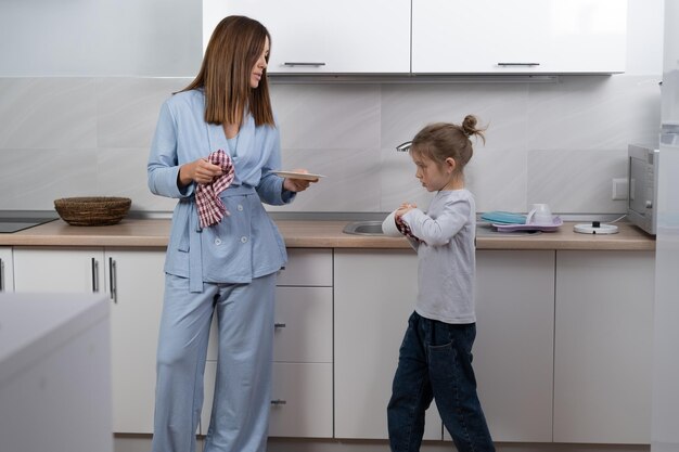 Maman et sa fille en apparence européenne sèchent la vaisselle dans la cuisine en les essuyant avec un torchon de cuisine Les parents aident le concept Copier l'espace