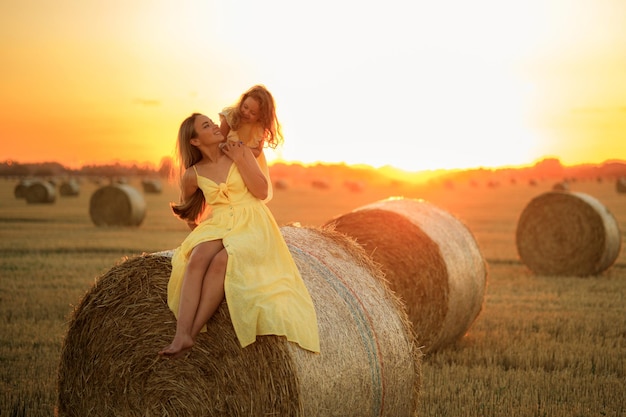 Maman et sa fille blonde sont assises sur une botte de foin dans un champ au coucher du soleil Mère et enfant s'amusent à la ferme
