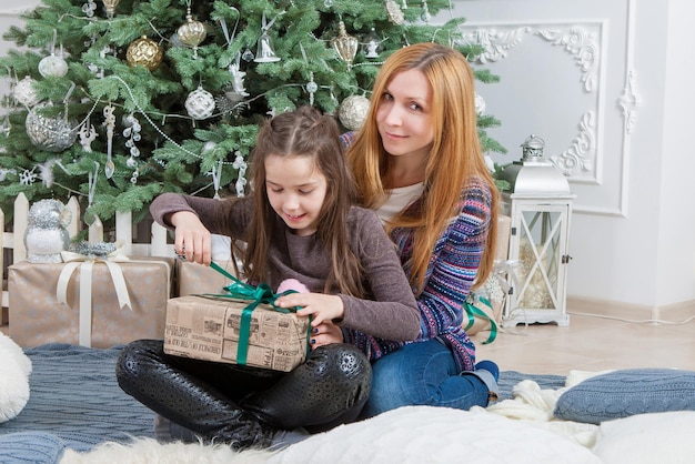 Maman avec sa fille avec un cadeau près du sapin de Noël