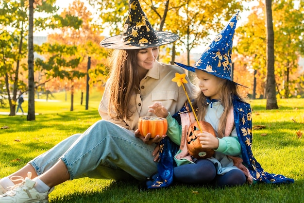 Maman et sa fille en costumes et chapeaux de sorcière dans le parc ensemble tromper ou traiter Happy Halloween