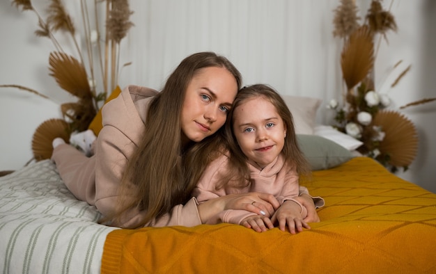 Maman et sa fille en costumes identiques sont allongées sur le lit et regardent la caméra