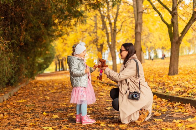 Maman et sa fille dans des vêtements à la mode avec un appareil photo se promènent dans un parc d'automne avec un feuillage jaune vif