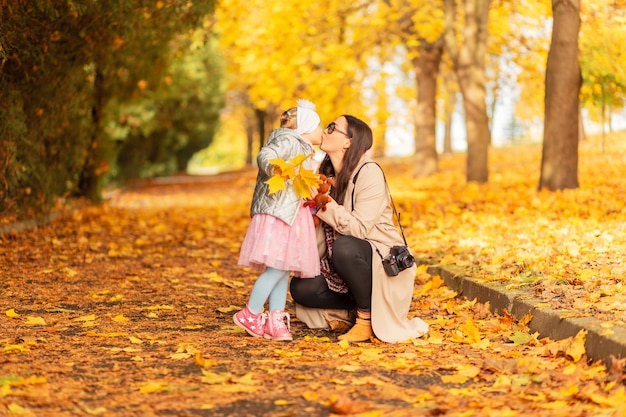 Maman et sa fille dans des vêtements à la mode se promènent dans le parc et font un baiser sur fond de feuillage d'automne jaune