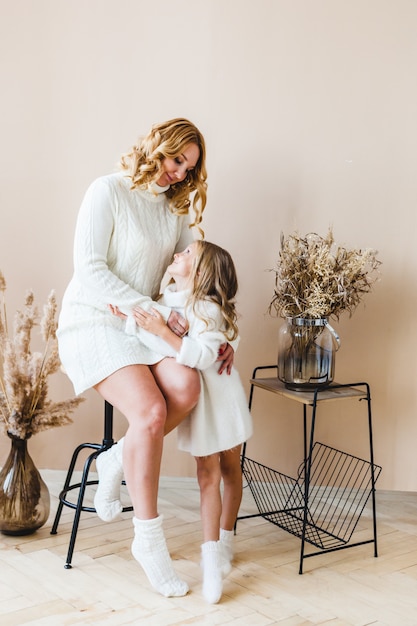 Maman et sa fille sur fond beige en pulls blancs