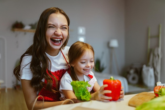 Maman et sa fille isolées à la maison trient les légumes dans la cuisine et s'amusent les unes avec les autres