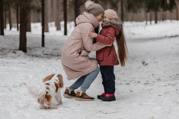 Maman et sa fille jouent dans une forêt enneigée avec leur chien