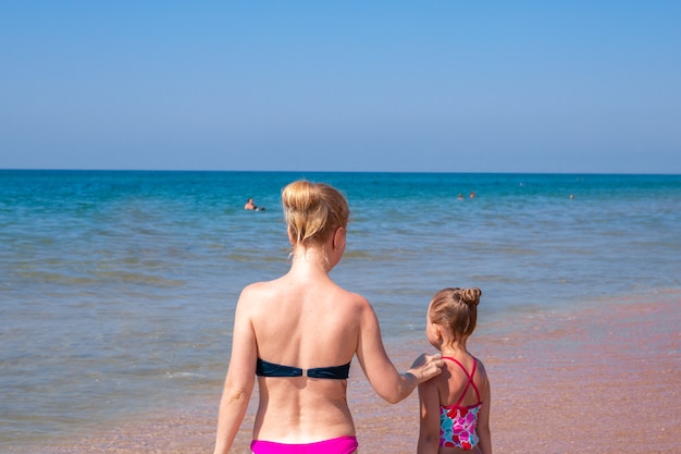 Maman et sa fille en maillot de bain se tiennent sur le rivage et regardent la mer. Vacances d'été en famille.