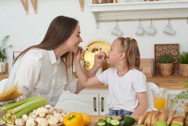 Maman et sa fille mangent des concombres et rient. Une bonne nutrition à la maison. Passer du temps ensemble