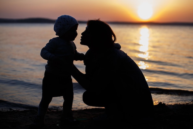 Maman et sa fille sur la plage en regardant le coucher du soleil s'embrasser et s'embrasser