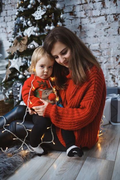 Maman avec sa fille en pulls chauds rouges saute sur le lit. Bonne maternité. Relations familiales chaleureuses. Intérieur de Noël et du nouvel an. Amour. Notion de famille.