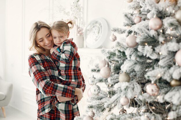 Maman et sa fille en pyjama à carreaux se serrant près de l'arbre de Noël