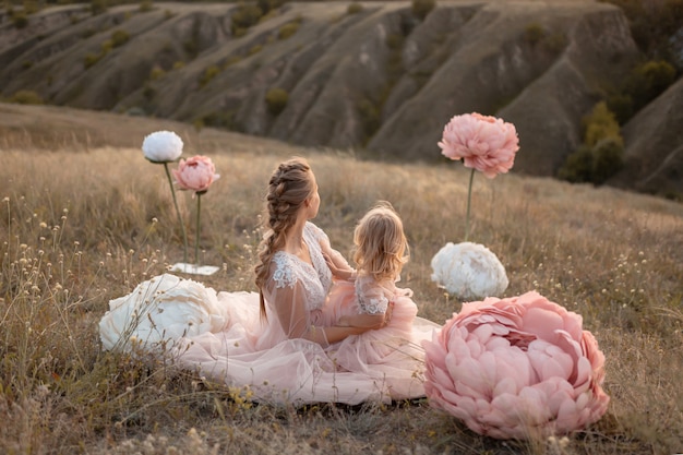 Maman et sa fille en robes de conte de fées roses jouent dans un champ entouré de grandes fleurs décoratives roses