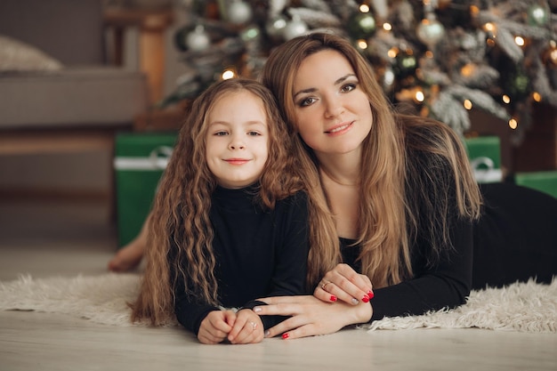 Maman et sa fille s'embrassent et posent à Noël à côté d'un arbre de Noël et de cadeaux Une famille heureuse dans une salle décorée du Nouvel An passe un bon moment