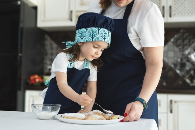 Maman et sa fille saupoudrent de biscuits avec du sucre en poudre