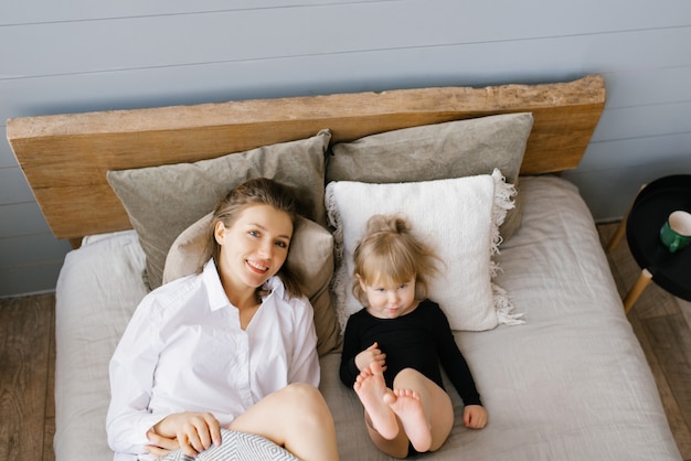 Maman et sa fille sont allongées sur le lit, se serrent dans leurs bras et sourient. Temps en famille à la maison