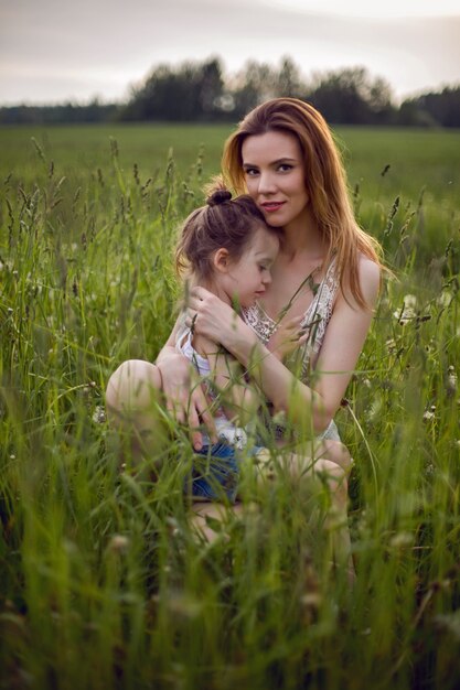 Maman et sa fille sont assises dans un champ vert en t-shirt blanc