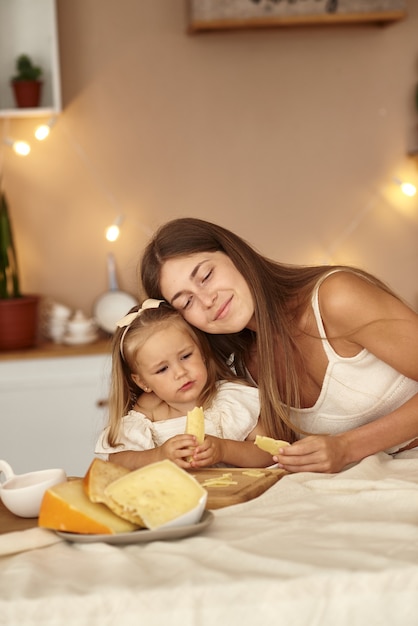 Maman et sa fille sont assises dans la cuisine et mangent un morceau de fromage.