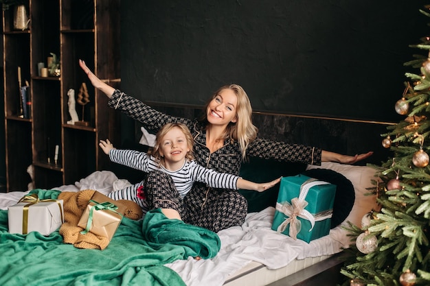 Maman et sa fille sont assises en pyjama sur le lit près de l'arbre de Noël à Noël Nouvel An cadeaux de vacances en famille autour de noël matin de famille