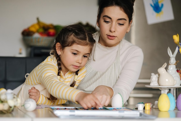 Maman et sa jolie petite fille assise à table dans la cuisine et colorient l'image avec des crayons