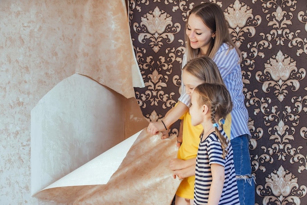 Maman et ses filles retirent ensemble le vieux papier peint des murs