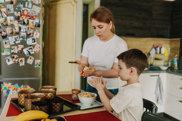 Maman avec ses petits fils à table dans la cuisine à la maison préparant ensemble la pâte pour la cuisson d'un gâteau de vacances