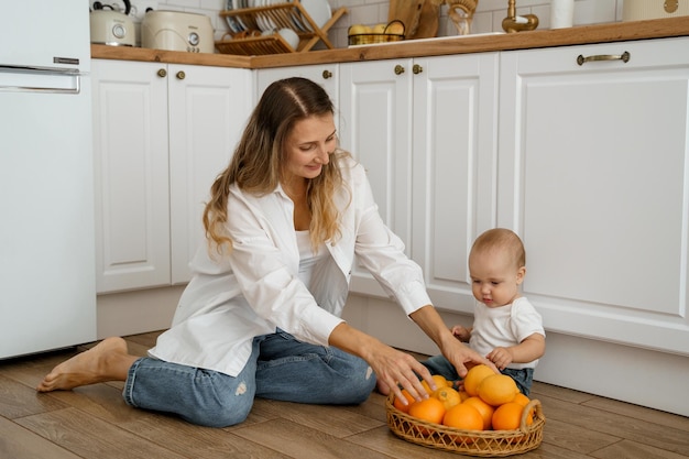 maman sur le sol de la cuisine avec un bébé et un panier de fruits lui donne une orange