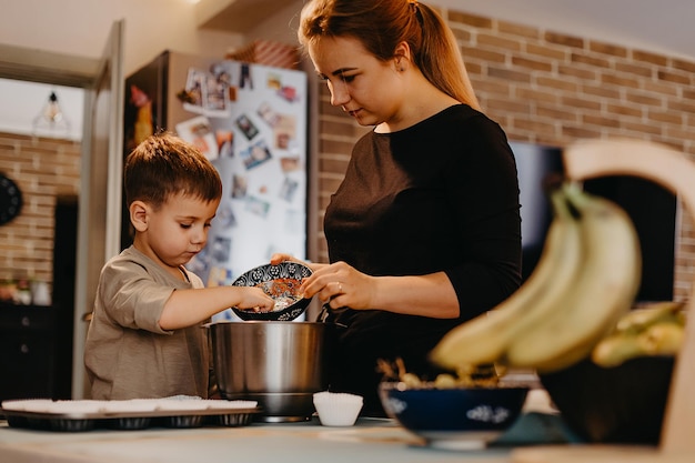 Maman et son fils aident à préparer des cupcakes dans la cuisine Le garçon avec du plâtre sur la main mélange la pâte et la met dans des moules à pâtisserie et maman raconte