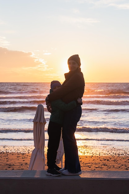 Maman et son fils profitent du coucher de soleil sur la mer avec un bel horizon. Merveilles de la nature. Beau paysage de la mer d'hiver.