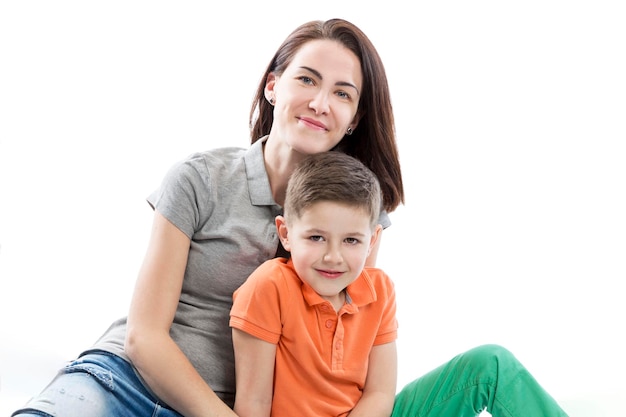 Maman et son fils sourient et s'étreignent Une brune en polo gris et jeans un enfant de 67 ans en T-shirt orange et pantalon vert Amour et tendresse dans la famille Isolé sur fond blanc