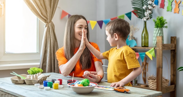 Maman et son petit fils ensemble colorent des œufs en s'amusant et en donnant cinq l'un à l'autre Concept de préparation familiale pour l'ambiance printanière festive de Pâques