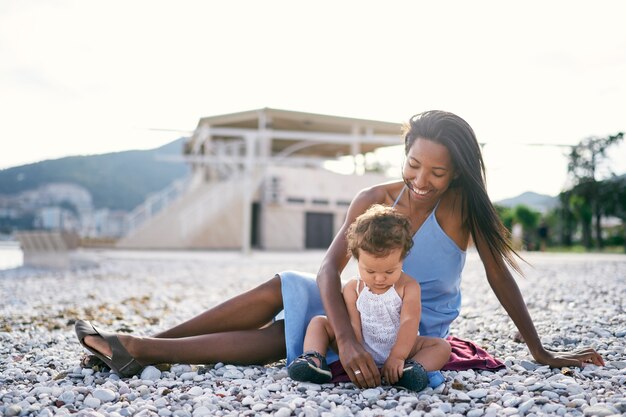 Maman souriante assise sur une couverture sur la plage à côté d'une petite fille