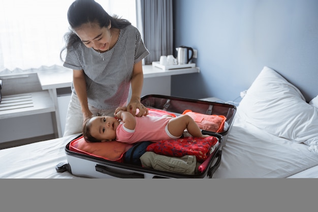 Maman sourit tenant un joli bébé couché dans une valise ouverte remplie