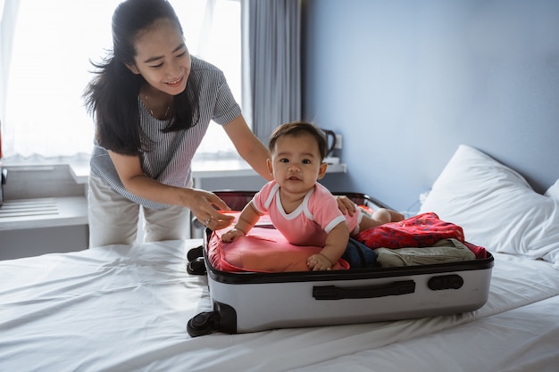 Maman sourit tenant un joli bébé couché dans une valise ouverte remplie