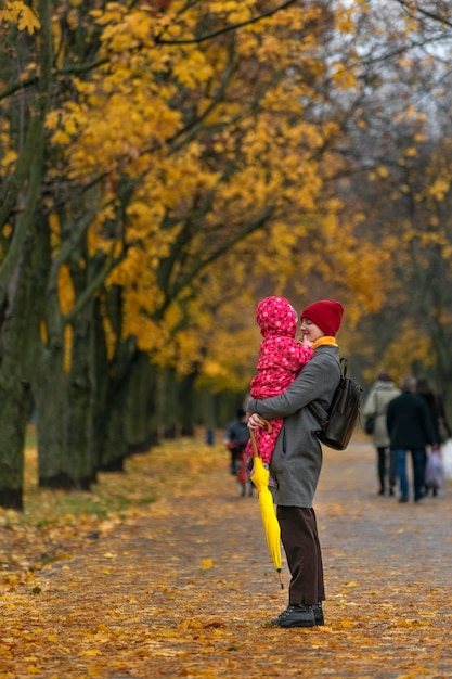 Maman tient le bébé dans ses bras dans le contexte d'un parc d'automne Marcher avec des enfants Cadre vertical