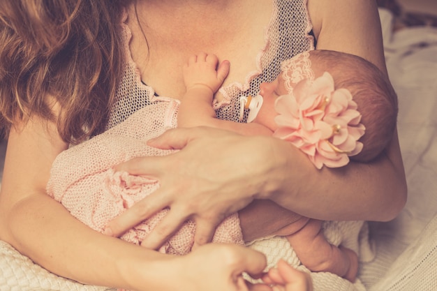 Photo maman tient dans ses bras son adorable bébé nouveau-né endormi et la regarde.