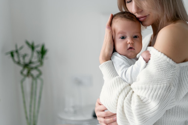 Maman tient un nouveau-né dans ses bras et appuie sa tête contre sa poitrine. Femme et enfant dans la chambre sur fond blanc. Concept de maternité et d'enfance.