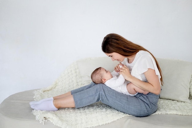 Maman tient une petite fille nouveau-née à la maison sur un canapé blanc et l'embrasse Amour maternel et espace de soins pour le texte