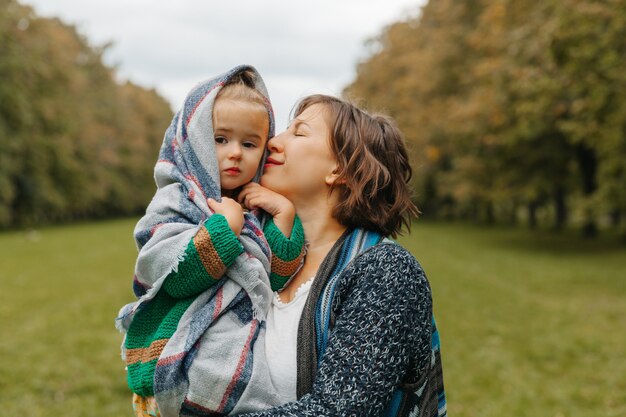 Maman tient sa fille dans ses bras dans le parc. femme avec un petit enfant marche dans le parc en automne. automne.