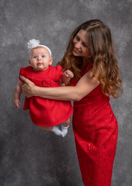 Maman tient sa petite fille dans ses bras Toutes deux portent des robes rouges Tournage en studio Tendresse