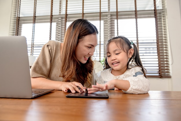 Maman travaille et enseigne à sa fille pour l'apprentissage en ligne à la maison. Mode de vie familial et nouvelle normalité après Covid-19.