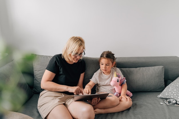 Mamie et fille d'âge préscolaire utilisant une tablette ensemble à la maison sur le canapé temps de convivialité familiale