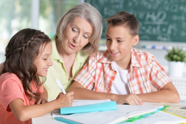 Mamie avec petits-enfants à faire leurs devoirs, à la maison ensemble