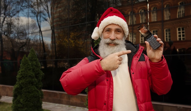 Man avec barbe en bonnet rouge présentant quelque chose d'extérieur. Noël. Nouvel An.