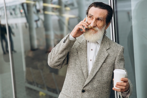 Man avec une barbe grise et une moustache dans une veste parle sur un téléphone et boire un café