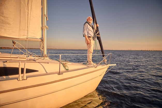 Man debout sur le côté d'un voilier ou d'un pont de yacht flottant en mer en regardant l'horizon