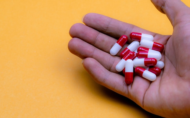 Man hand holding redwhite comprimés capsule sur fond jaune Médicament sur ordonnance Pharmaceutic