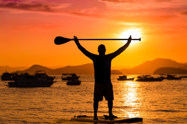 Man holding paddle sur le dessus en se tenant debout au coucher du soleil