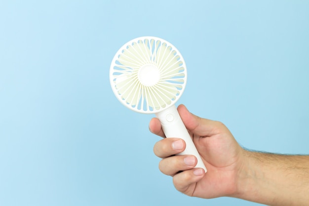 Man holding petit ventilateur usb portable close-up isolé sur fond bleu